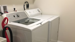 A compact, white front-loading washer and dryer unit with a red hose attached, situated in a laundry room with a patterned rug on the floor. - Cozy Retreat • King Bed & Kitchen Near Lee (Cleveland)
