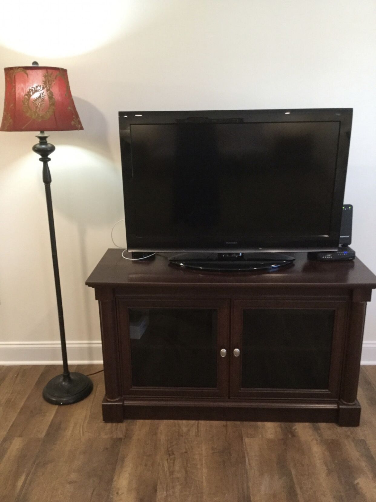 Un televisor de pantalla plana sobre un mueble de madera con dos puertas, un control remoto y una lámpara a un lado.