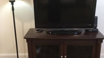 Un televisor de pantalla plana sobre un mueble de madera con dos puertas, un control remoto y una lámpara a un lado.
