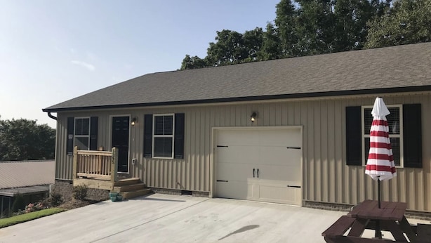 A single-story building with a garage door, a small porch with steps, and a picnic table with an umbrella. - Cozy Retreat • King Bed & Kitchen Near Lee (Cleveland)