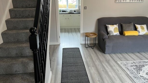 Una escalera que lleva a una zona de cocina con un sofá gris y una alfombra en la sala.
