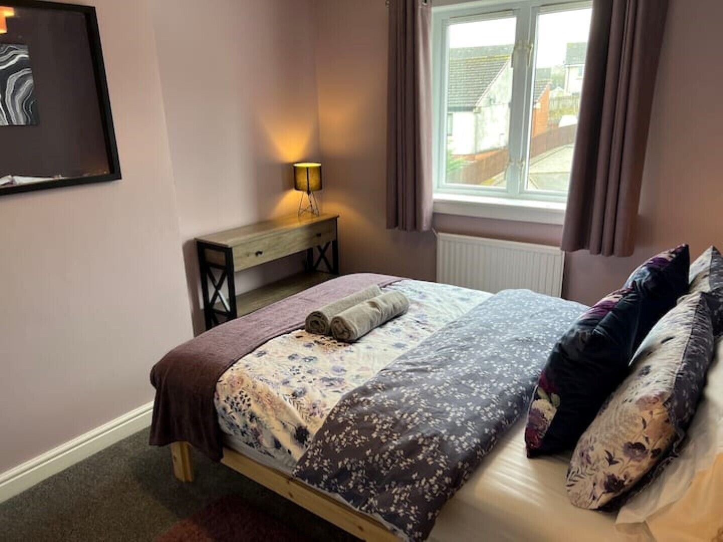 Ein ordentlich eingerichtetes Schlafzimmer mit Bett, Nachttisch, Lampe und einem Fenster mit Vorhängen.