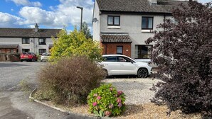 Un barrio residencial con casas, un coche estacionado y un jardín con flores rosas.
