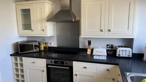 Una cocina con armarios blancos, una campana extractora de acero inoxidable, microondas, tostadora y panera.