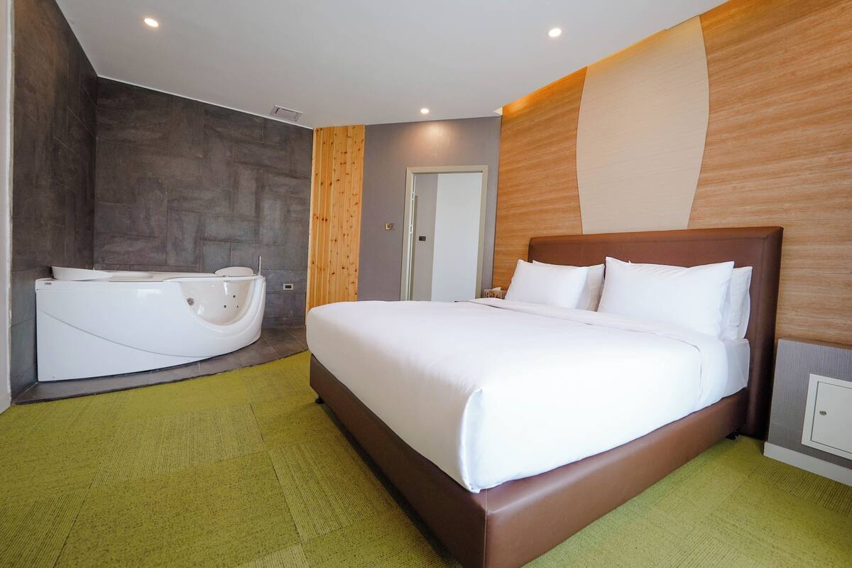 Une chambre d’hôtel moderne avec un grand lit, une baignoire séparée et une moquette verte.