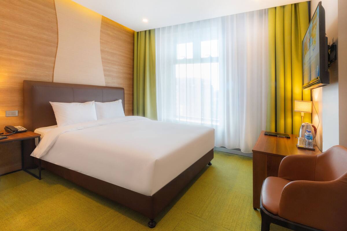 Une chambre d’hôtel équipée d’un lit, d’un bureau, d’une chaise, d’une télévision et d’une fenêtre avec des rideaux.