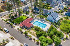 An aerial view of a residential area with a large house featuring a swimming pool, surrounded by lush greenery and other houses.