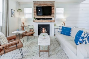 A living room with a fireplace, a television mounted above it, and a white sofa with blue pillows.