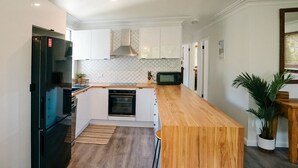 A modern kitchen with white cabinets, a black refrigerator, a microwave, and a wooden countertop. - Tallowood Treehouse  (East Ballina)