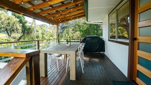 A covered outdoor patio with a wooden table and chairs, a barbecue grill, and a view of greenery. - Tallowood Treehouse  (East Ballina)