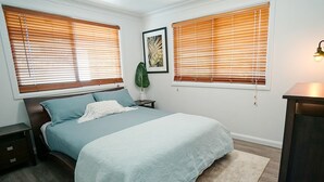 A bedroom with a bed, nightstands, a plant, and a wall-mounted lamp. - Tallowood Treehouse  (East Ballina)