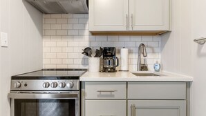 Una cocina con armarios blancos, una estufa de acero inoxidable, una cafetera y un lavabo.