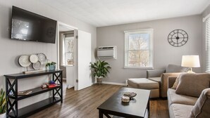 Una sala de estar con televisión, un reloj, un sofá, una mesa de centro y una planta.