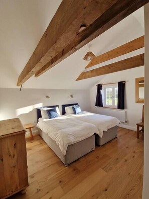 Une chambre avec deux lits, des poutres en bois, une fenêtre avec des rideaux et une commode en bois.