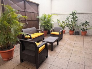 An outdoor patio area with wicker furniture, yellow cushions, and various potted plants. - Inari Guatemala (Guatemala City)