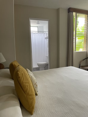 A hotel room with a bed, a window with curtains, a bathroom visible through an open door, and a chair. - Inari Guatemala (Guatemala City)