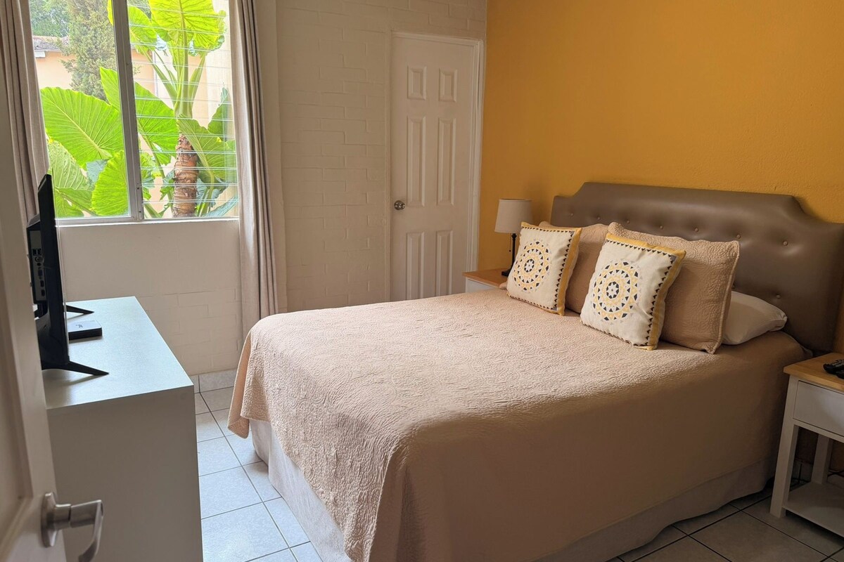 A bedroom with a bed, a bedside table, a lamp, and a window with curtains.