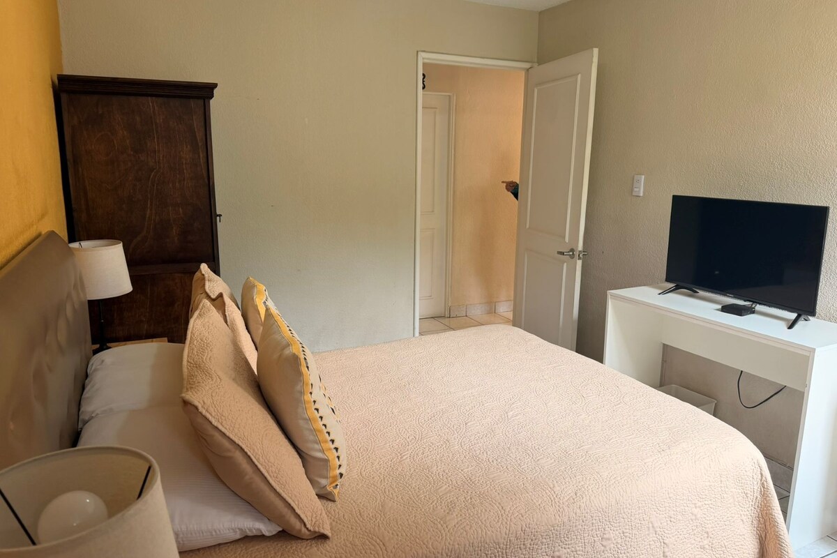 Habitación de hotel con cama, escritorio con televisor, armario y puerta que da a otra habitación.