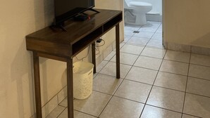 A room with a wooden TV stand, a white bucket, and a bathroom visible through an open door. - Inari Guatemala (Guatemala City)