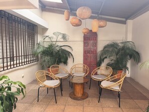 Un patio con sillones de mimbre, una mesa redonda y lámparas colgantes de ratán.