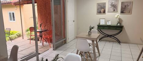 A room with a dining area, a small table with chairs, a green console table with a vase and a QR code, and a wall with framed artwork.