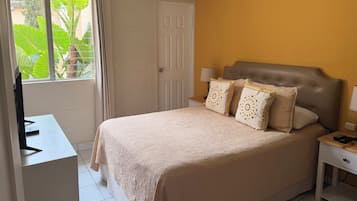 Un dormitorio con cama, mesita de noche, lámpara y ventana con cortinas.