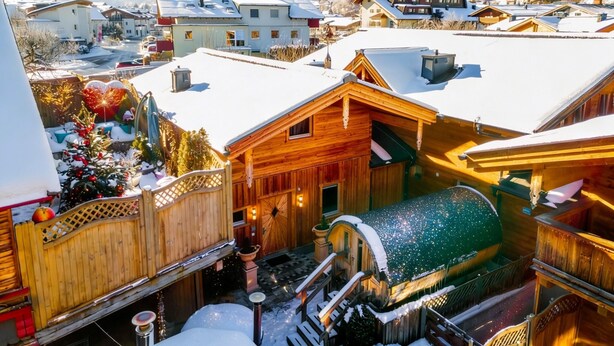 Uma aldeia coberta de neve com edifícios de madeira, um teleférico de esqui e montanhas ao fundo.