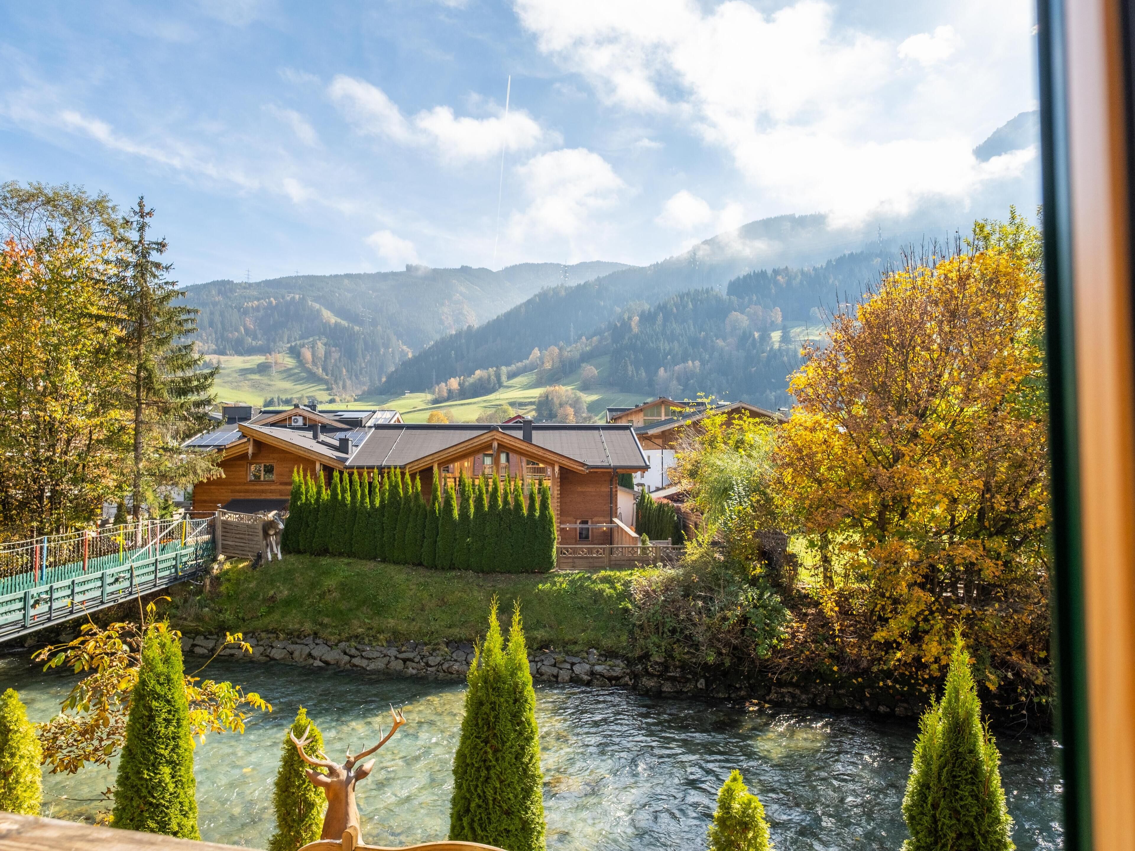 A wooden cabin with a river view, surrounded by trees and mountains.