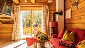 A cozy cabin interior with a red sofa, a wooden coffee table with gold bars, and a fireplace. - Riverside chalet with terrace and sauna in Kaprun (Kaprun)