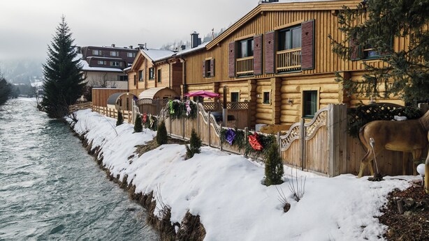 A wooden cabin with a river view, a wooden deck, and a snow-covered landscape. - Riverside chalet with terrace and sauna in Kaprun (Kaprun)