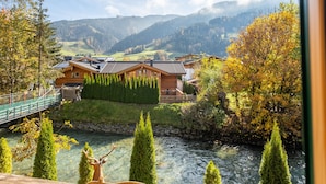 A view of a riverside property with wooden cabins, a bridge, and a mountain backdrop. - Riverside chalet with terrace and sauna in Kaprun (Kaprun)