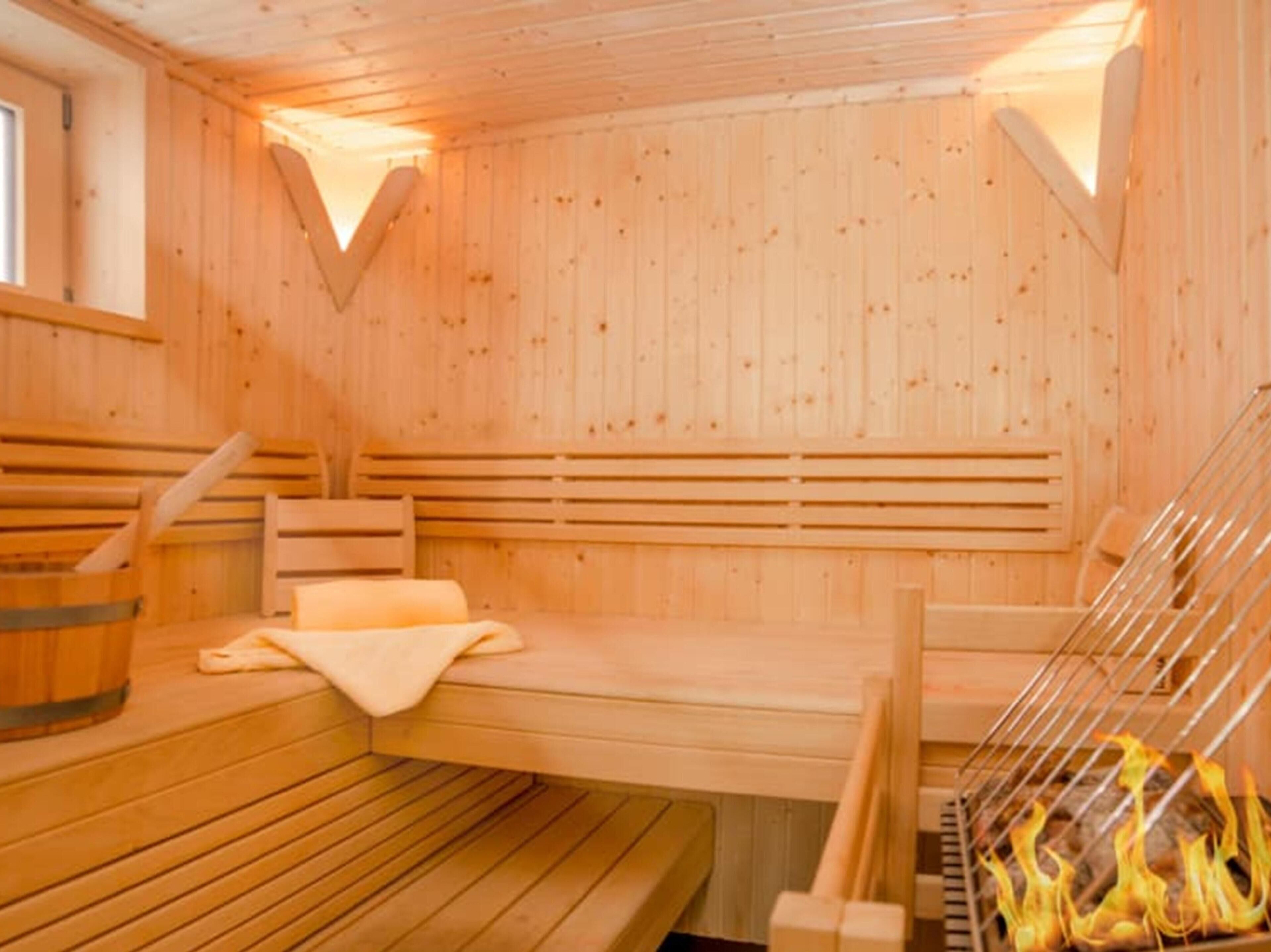 Una sauna in legno con panche, una panca con un asciugamano e una griglia con legna ardente.