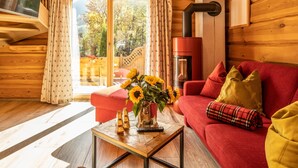 A cozy cabin interior with a red sofa, a coffee table with a vase of sunflowers, and a fireplace. - Group house with sauna in the heart of Kaprun (Kaprun)