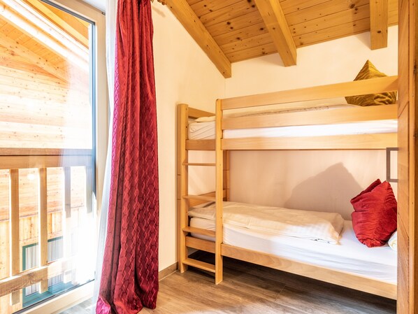 A bunk bed room with a wooden ceiling and a window with red curtains.
