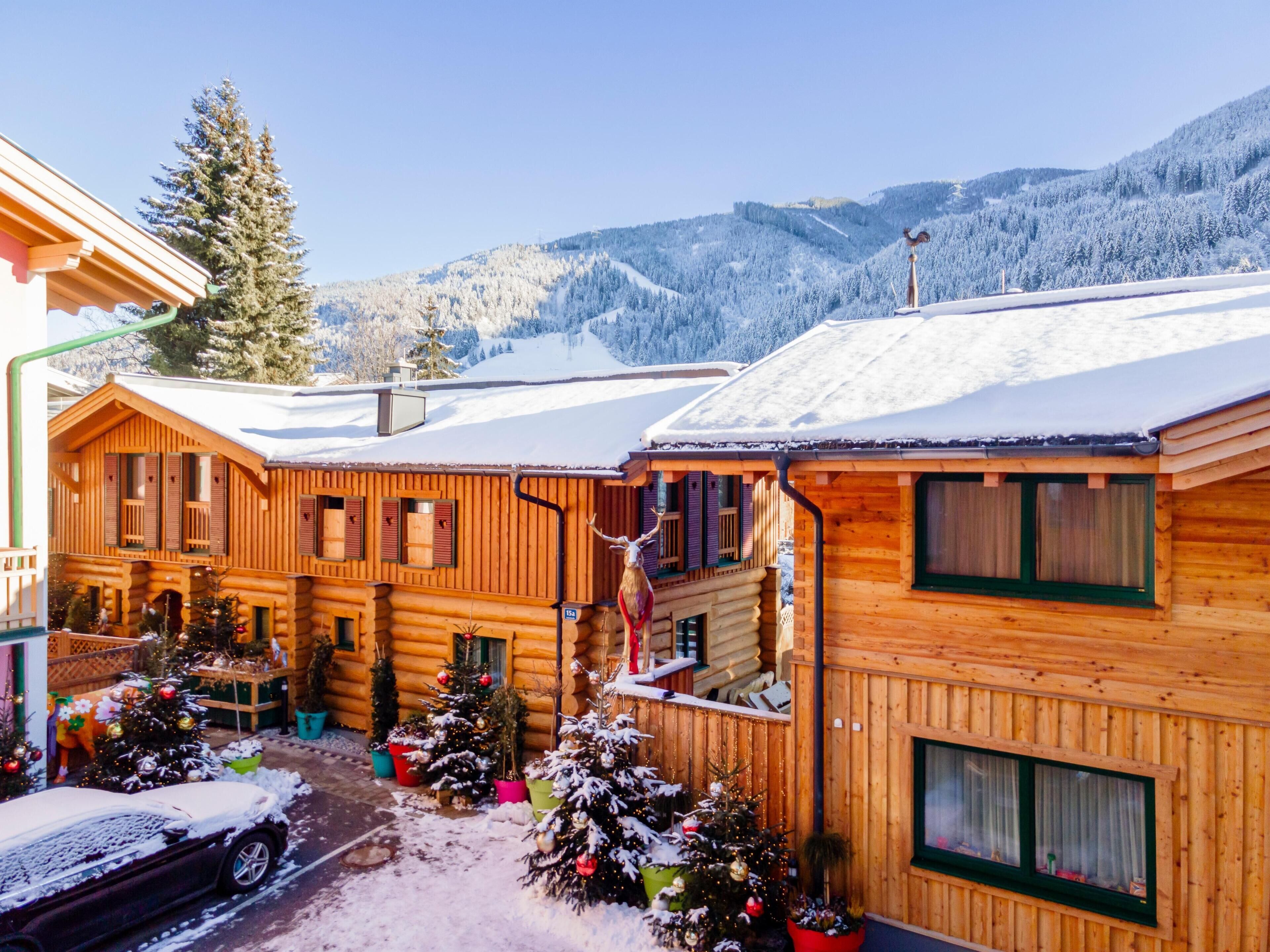 A log cabin hotel with multiple wooden buildings, snow-covered surroundings, and a view of snow-covered mountains.