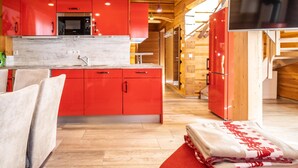 A modern kitchen with red cabinets, a built-in microwave, and a large TV. - Group house with sauna in the heart of Kaprun (Kaprun)