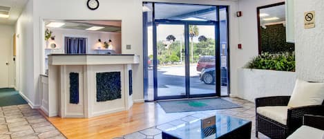 A hotel lobby with a reception desk, seating area, and a view of the street through glass doors.