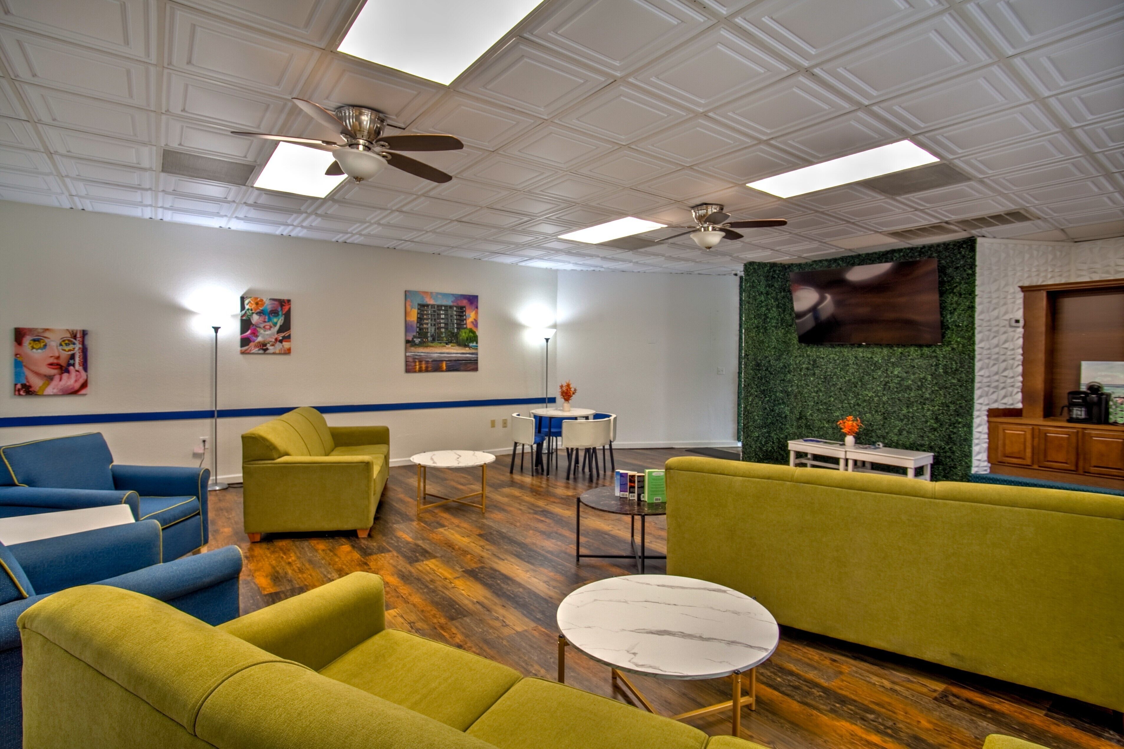 Un espace de détente moderne avec des canapés verts et bleus, une machine à café et un téléviseur à écran plat fixé au mur.