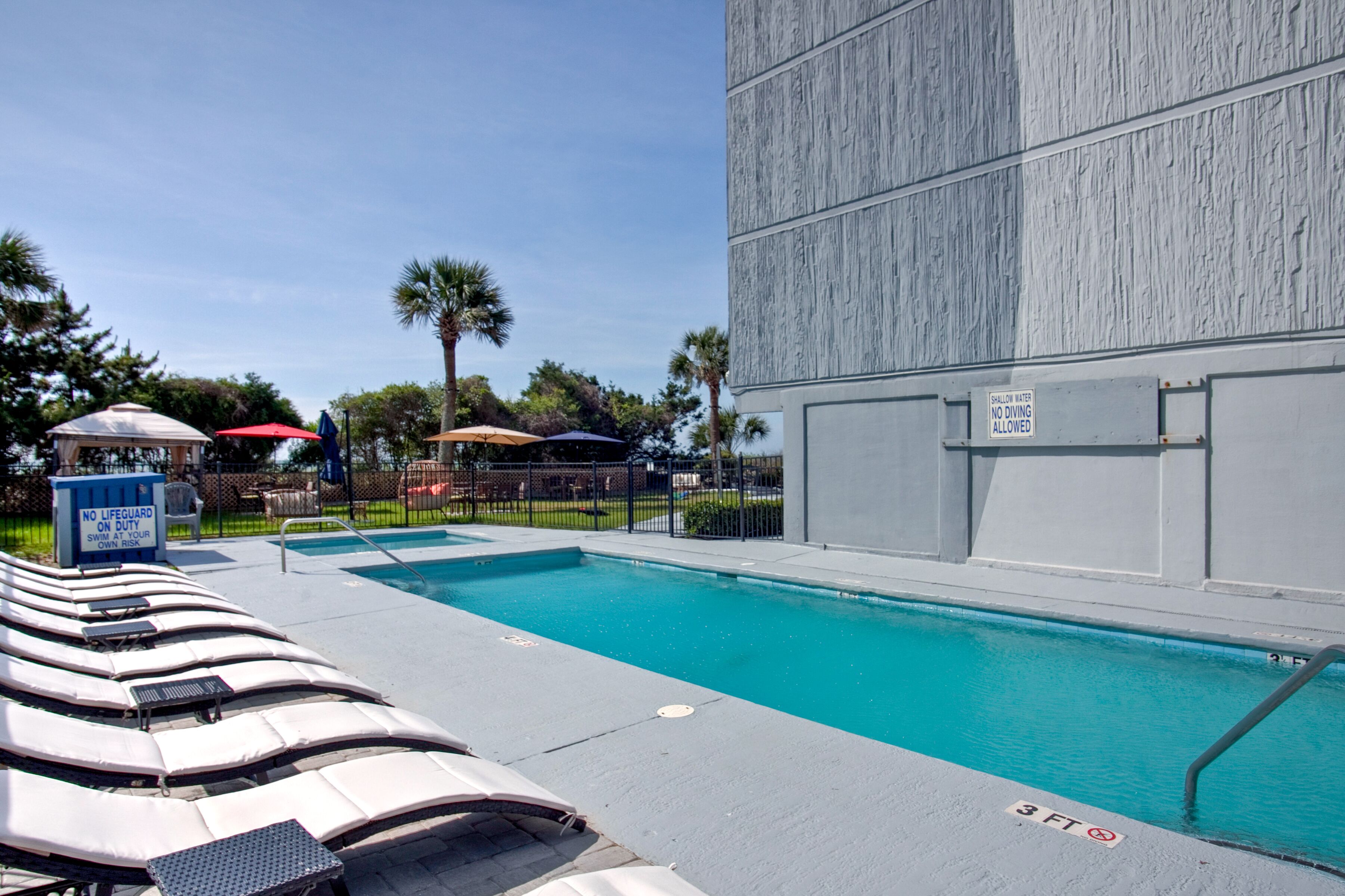 A swimming pool with lounge chairs, a no diving sign, and a lifeguard duty sign.