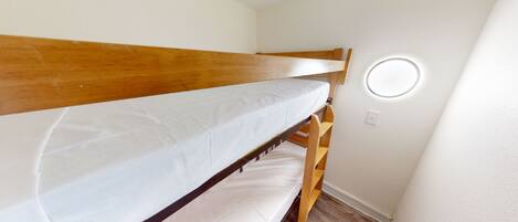 A bunk bed with a wooden frame and white bedding in a room with white walls and a wooden floor.