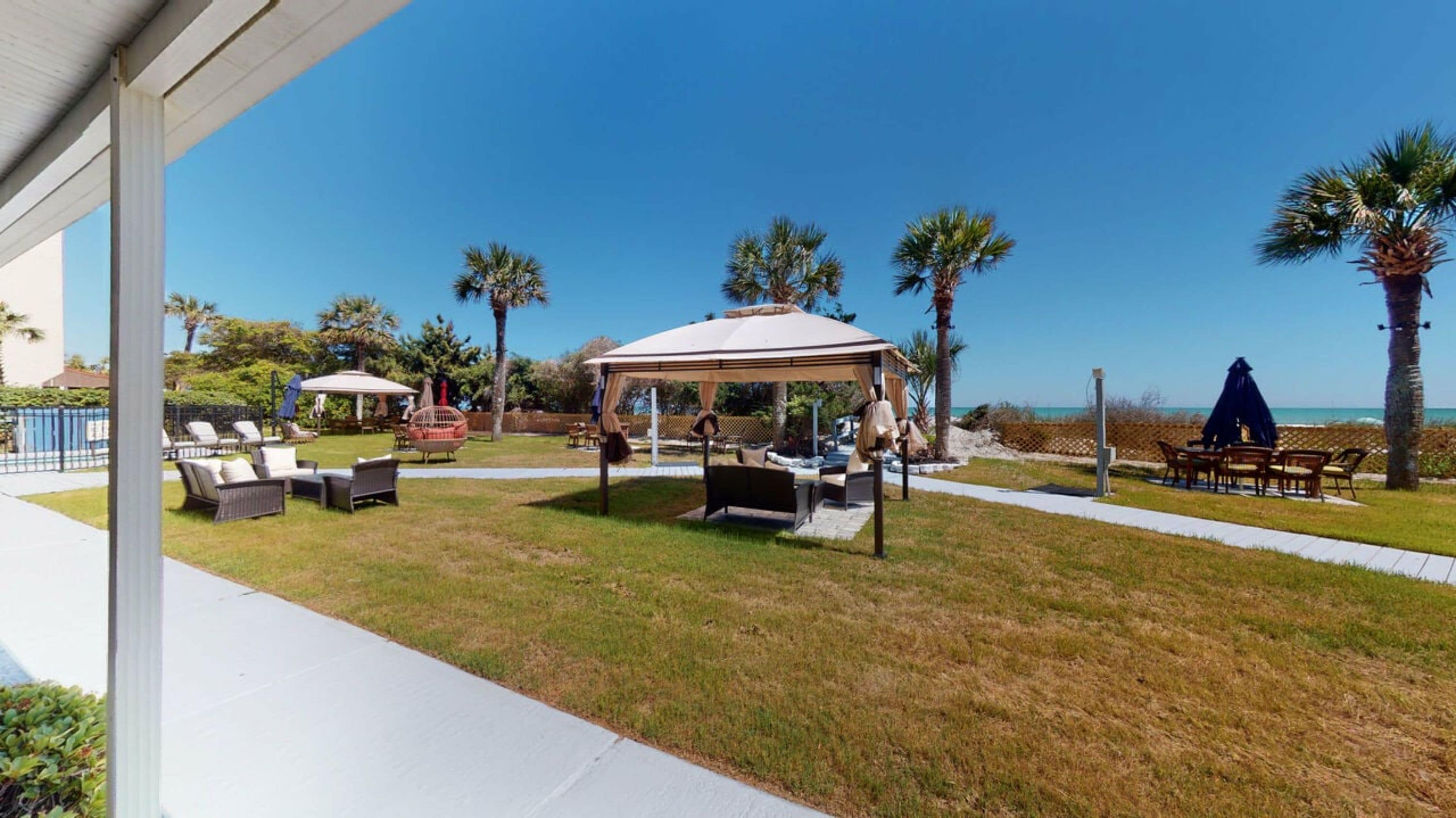 A covered outdoor seating area with tables and chairs, a gazebo, and palm trees.