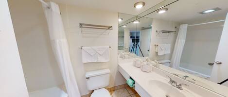 A modern bathroom with a bathtub, toilet, and sink. There is a large mirror above the sink and a shower curtain.
