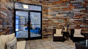 A modern interior with a stone wall, a blue sofa, wicker chairs, and a glass door leading outside. - Willow Bay Resort  (Myrtle Beach)