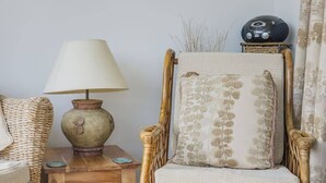 Een rieten stoel met een kussen, een houten bijzettafeltje met een lamp en een radio.