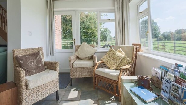 Een gezellige kamer met rieten stoelen, een tafel met folders en grote ramen met uitzicht op het landschap.