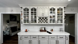 Una cocina con armarios blancos, encimera de mármol y una estantería empotrada para vinos.