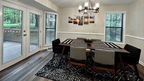 Un comedor con candelabro, una mesa con sillas y vistas al exterior a través de amplios ventanales.