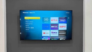 Un televisor de pantalla plana montado en una pared oscura, mostrando la interfaz de un servicio de transmisión con varios íconos de aplicaciones.