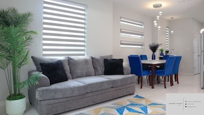 Una sala de estar con un sofá gris, sillas azules y una mesa de comedor.