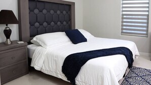 Un dormitorio moderno con un cabecero capitonado, una mesita de noche con una lámpara y una alfombra estampada.